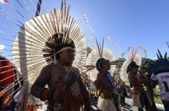 Three Indigenous people wearing large round feather headdresses