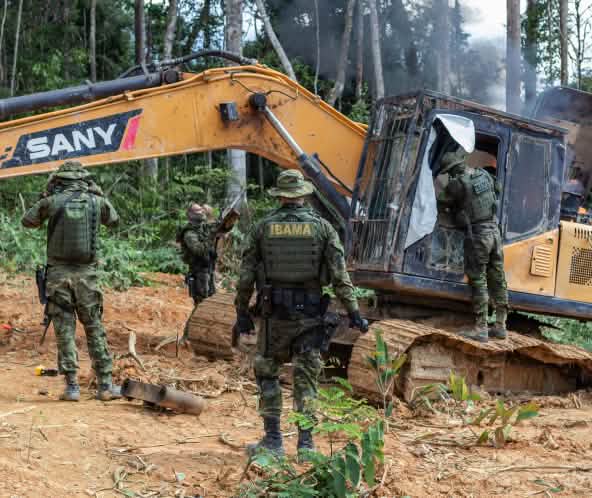 A group of men in camouflage suits from the environmental agency IBAMA disables a yellow excavator in the rainforest