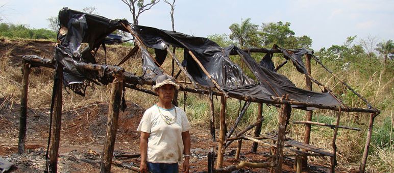 A Guarani woman infront of a burnt down hut