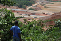 A farmer standing in the forest, looking at an open-pit mine