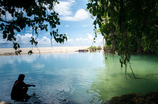 A woman is sitting in the water in a bay lined with rocks and a sandy beach