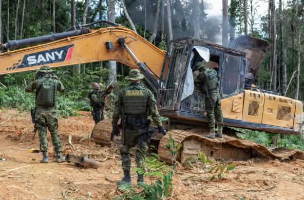 A group of men in camouflage suits from the environmental agency IBAMA disables a yellow excavator in the rainforest