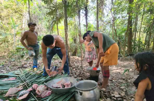 Four people prepare food in the forest in leaves and pots placed on the ground