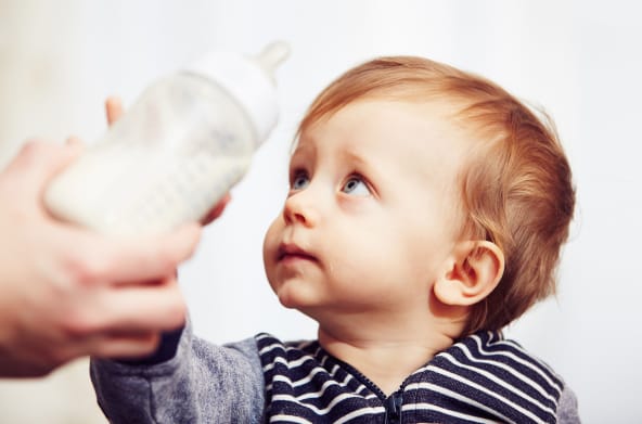 A worried-looking baby pushing its bottle away