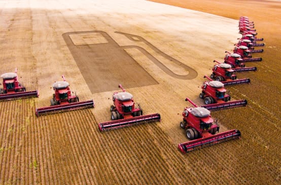 Photomontage: 15 combines in a wedge formation harvesting a soybean plantation. The outline of a gas pump can be seen in the harvested area.