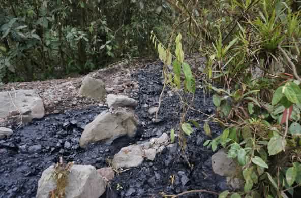 A stream of black crude oil has spilled over an area covered with gravel and stones