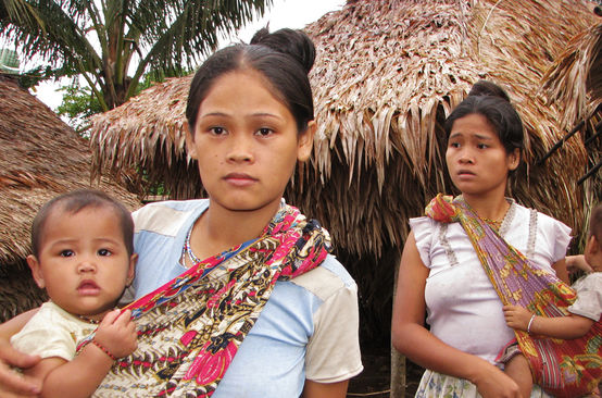 Two women with their children in front of thatched houses