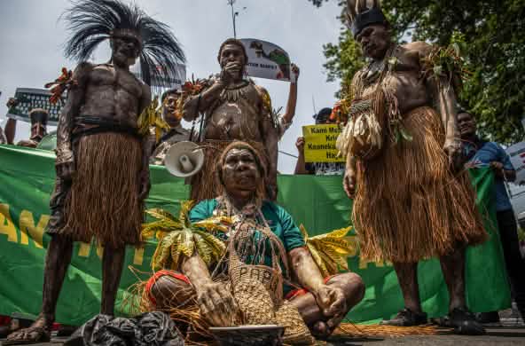Four Indigenous Papuans in traditional clothing in front of banner