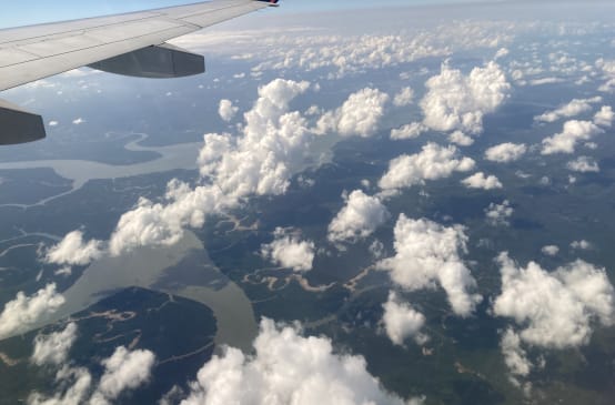 View of clouds, rivers and rainforest seen from an airliner, with the wing at the top of the frame