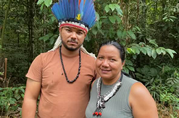 Portrait of an Indigenous woman wearing a feather necklace on the right and a young Indigenous man wearing a feather headdress on the left