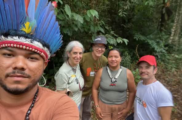 Selfie of an Indigenous person wearing a feather headdress on the left, with four people behind him in front of rainforest vegetation