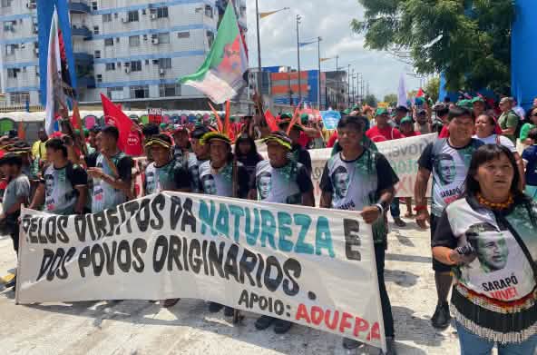 A group of around 15 Indigenous people with feather headdresses and a large banner