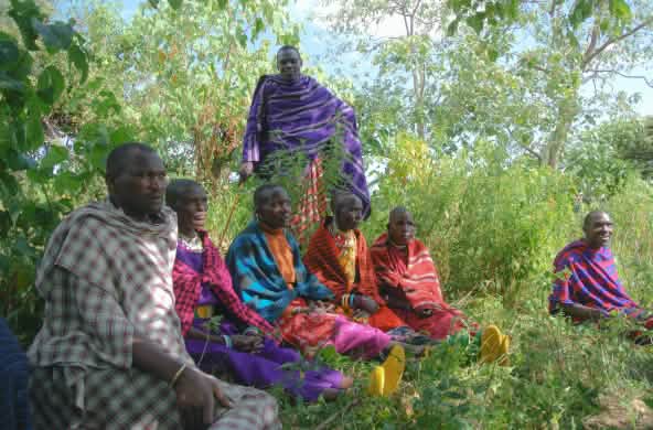 A group of colorfully dressed Maasai men sitting in the grass