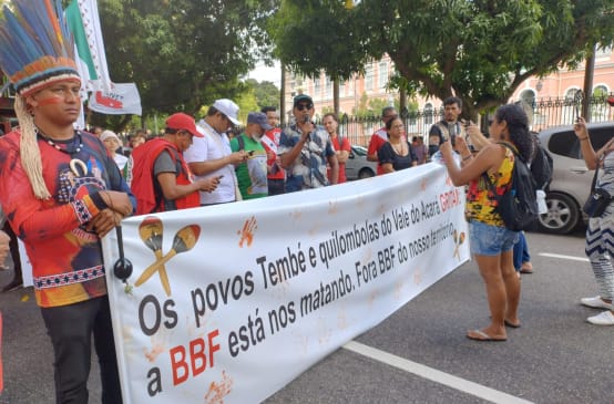 A group of indigenous people protest with a large banner on a street in a town: the banner reads: ‘The Tembé and Quilombola peoples of the Acará Valley are crying out. BBF is killing us. BBF out of our territory