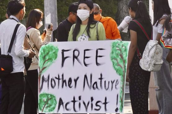 Young woman holding a large placard with the text “Free Mother Nature Activist!”
