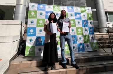 A woman and a man standing in front of a building entrance next to a banner reading “YASunidos,” holding documents in their hands