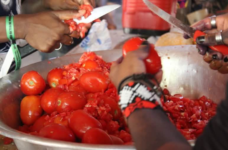 Close-up of two people’s hands cutting tomatoes over a metal bowl