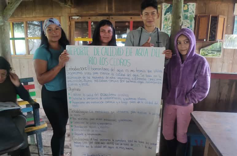 Four young people hold up a large sheet of paper on which they have written about water quality
