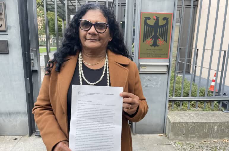 Quilombola woman Marli Borges holding a letter outside the barred entrance to the Federal Ministry for Economic Cooperation and Development (BMZ)