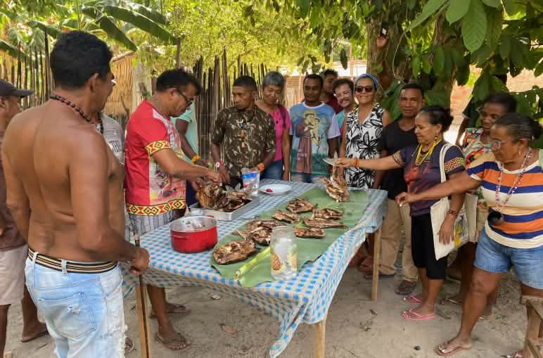 A group of 12 Indigenous people surround a table with grilled fish