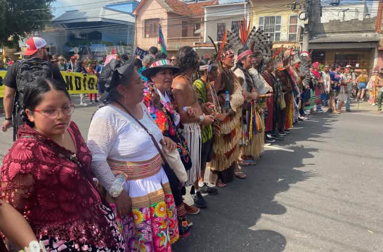Indigenous women and men dressed in colorful clothing form a line at a demonstration