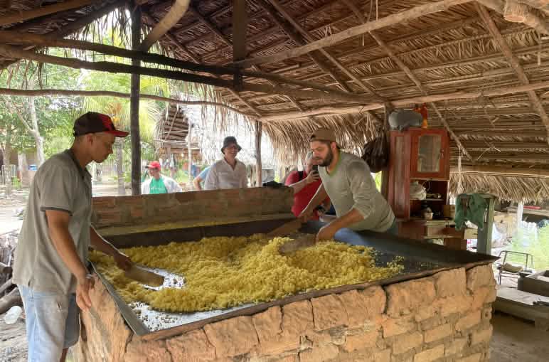 Two men roast cassava in a large square metal pan