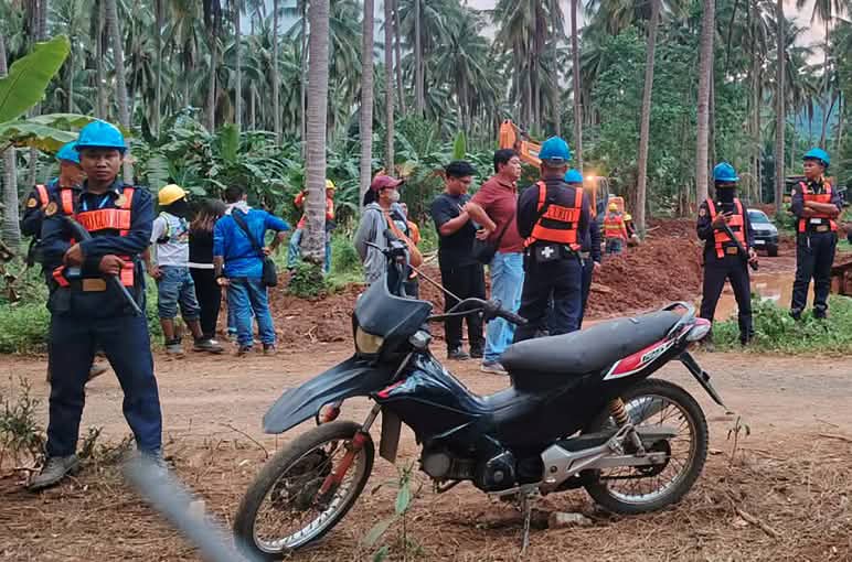 A motorbike in the foreground, with several armed guards behind and around it, standing among the local people