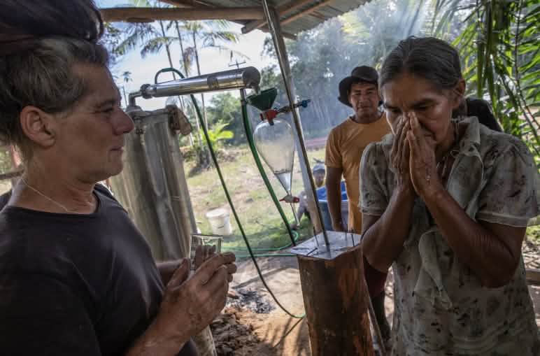 An Indigenous woman standing beside a steam distillation unit smells essential oils that the instructor has dripped onto her hand