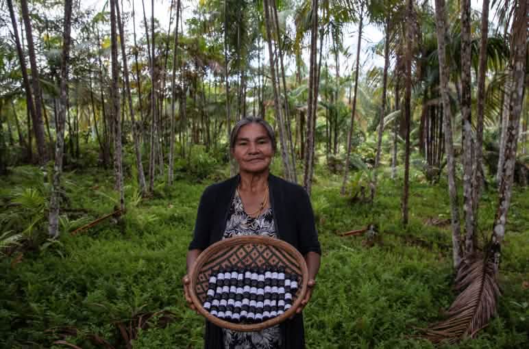 An Indigenous woman in the rainforest presents a basket filled with small bottles of essential oils