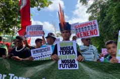 Indigenous people marching in a row holding up placards with slogans such as: “Our land is our future”