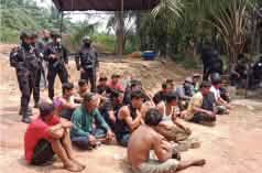 Detained Dayak people sit on the ground, armed police officers behind them