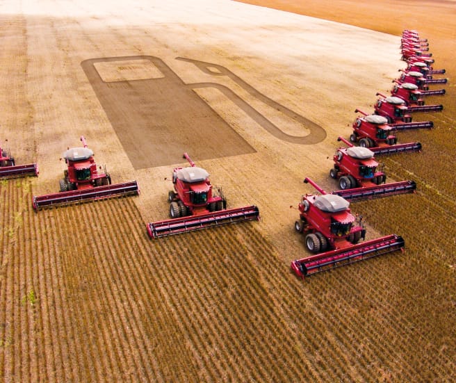 Photomontage: 15 combines in a wedge formation harvesting a soybean plantation. The outline of a gas pump can be seen in the harvested area.