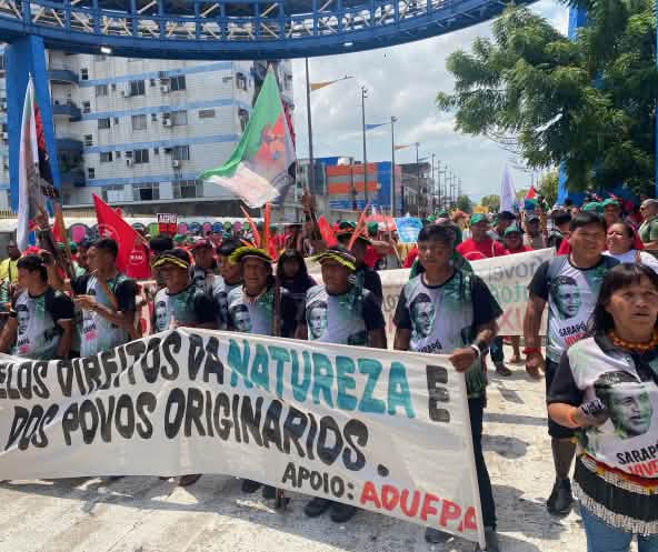 A group of around 15 Indigenous people with feather headdresses and a large banner