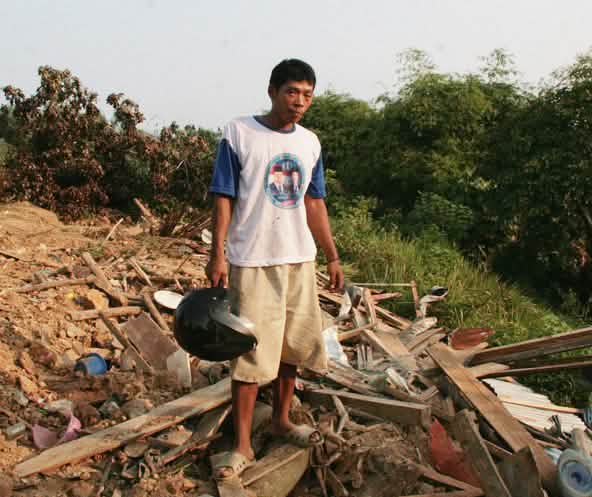 A farmer stands in front of the ruins of his village