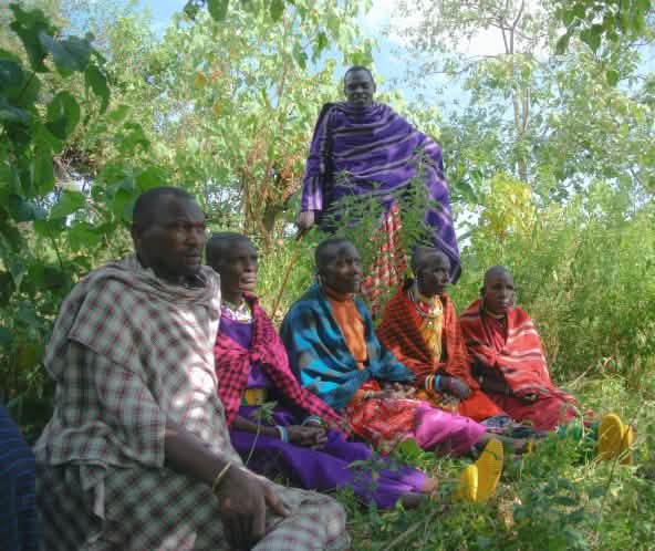A group of colorfully dressed Maasai men sitting in the grass
