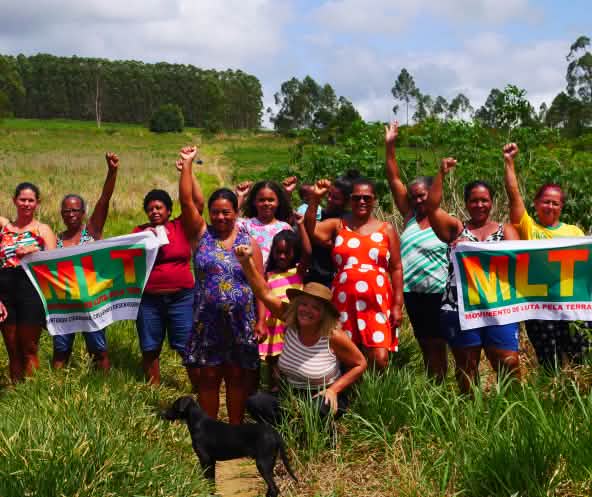 A group of 15 women is protesting with their fists raised and two banners bearing the letters MLT