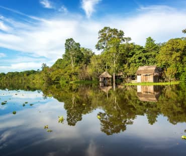 The Amazon rainforest and a wooden hut are reflected in the waters of the Yanayacu River in Peru