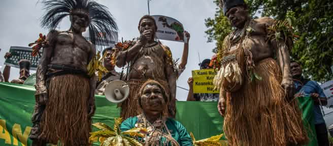 Four Indigenous Papuans in traditional clothing in front of banner