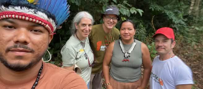 Selfie of an Indigenous person wearing a feather headdress on the left, with four people behind him in front of rainforest vegetation