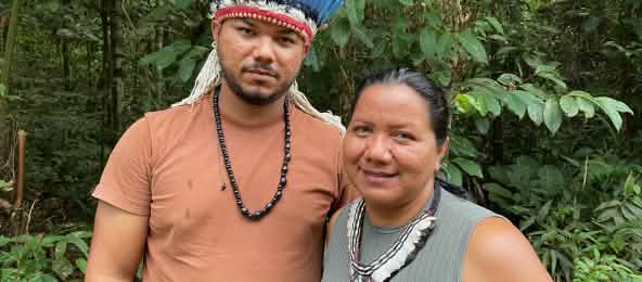 Portrait of an Indigenous woman wearing a feather necklace on the right and a young Indigenous man wearing a feather headdress on the left