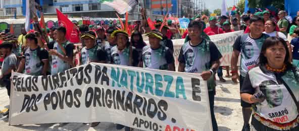 A group of around 15 Indigenous people with feather headdresses and a large banner