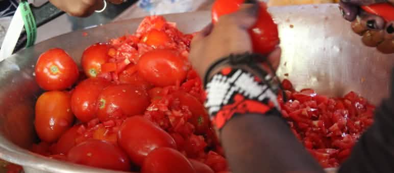 Close-up of two people’s hands cutting tomatoes over a metal bowl