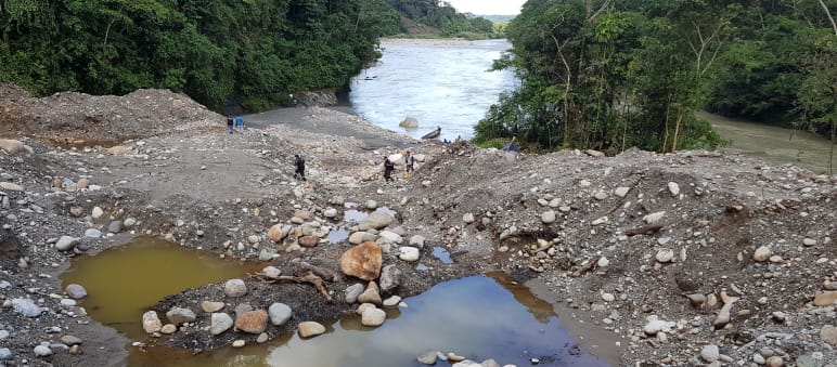 Excavated sediment and contaminated pools on a riverbank in the forest