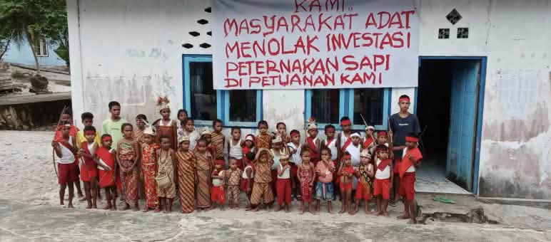 Children in front of a school and a banner reading “We Indigenous people reject investment in cattle ranching on our Indigenous land”