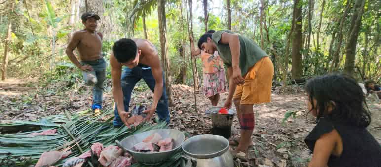 Four people prepare food in the forest in leaves and pots placed on the ground