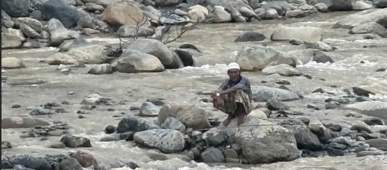 A man squatting on a boulder in the river