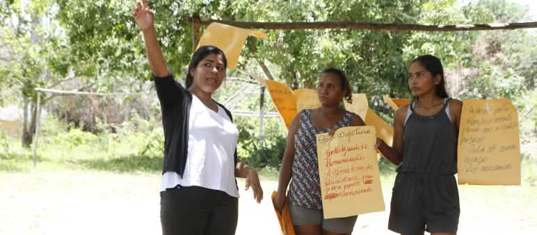 Three women hold up hand-painted posters