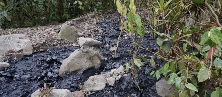 A stream of black crude oil has spilled over an area covered with gravel and stones