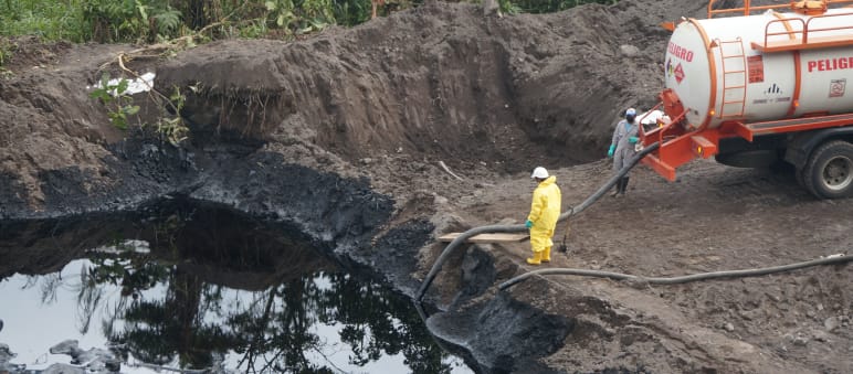 Two oil workers use a hose to suck crude oil from an earthen pond into a tanker truck