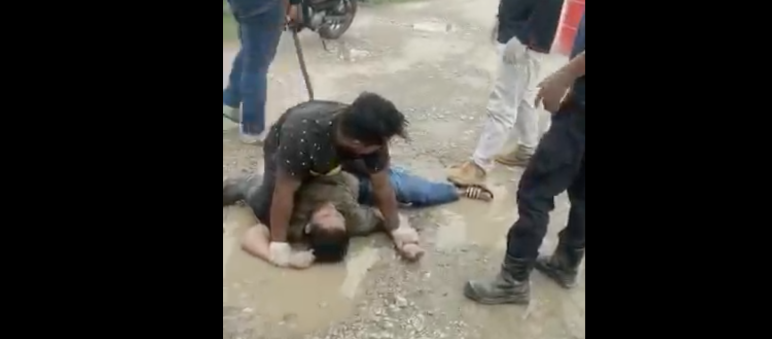 Scene from a video: one of the perpetrators stands behind the victim with a baton A villager is assaulted by plantation workers